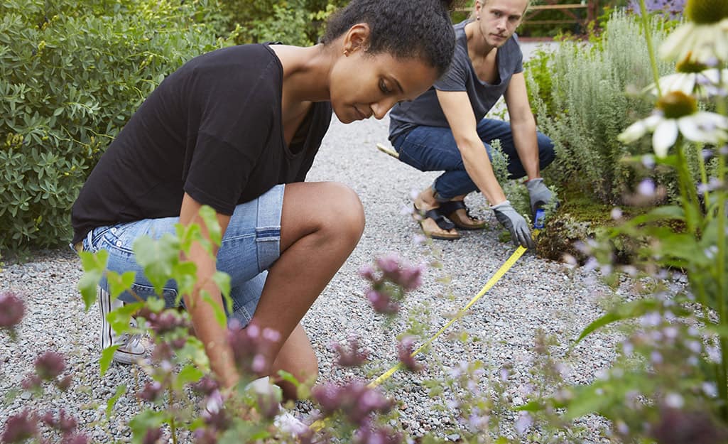 Two people using a steel measuring tape to measure a gravel garden path. Two people using a steel measuring tape to measure a gravel garden path.