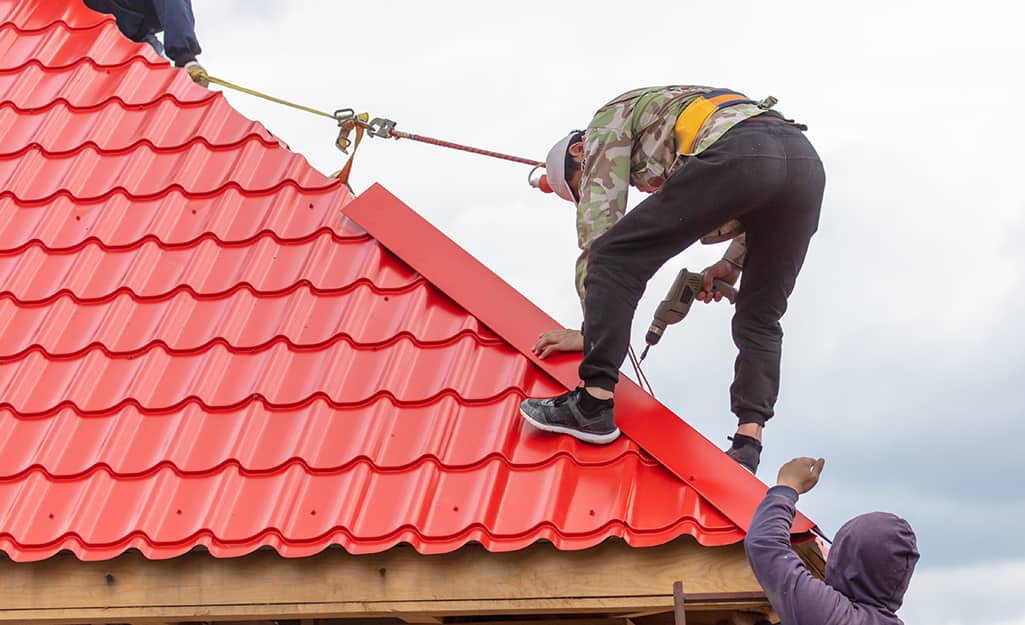 Two workers use safety gear to install a roof's ridge cap. Two workers use safety gear to install a roof's ridge cap.