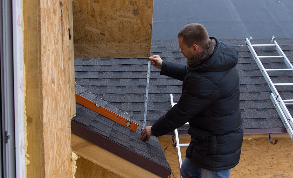 A man wears a winter coat while measuring a roof. A man wears a winter coat while measuring a roof.