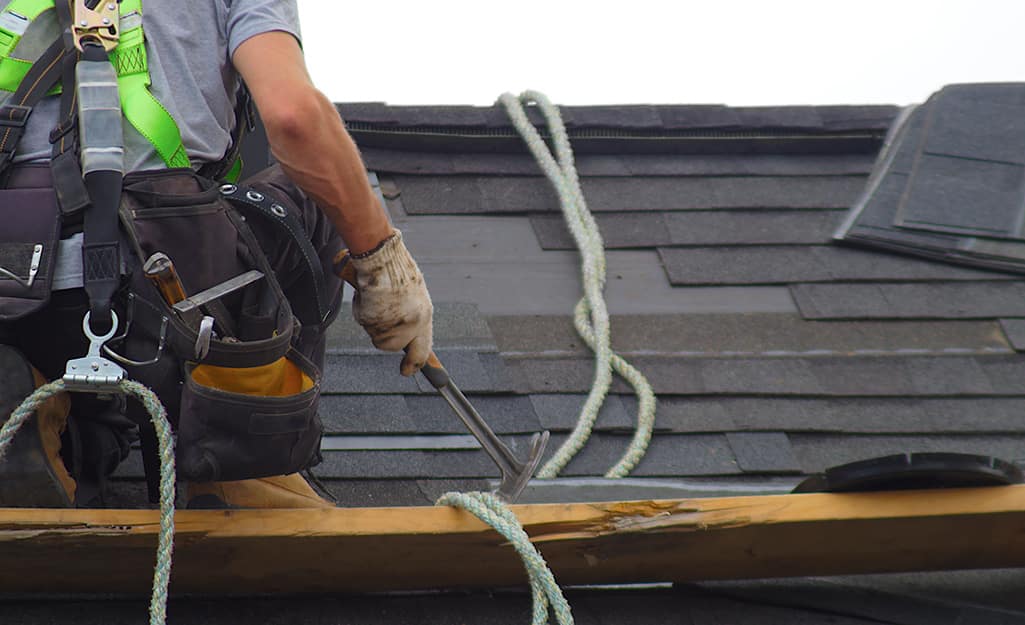 A person uses a hammer to remove old roofing. A person uses a hammer to remove old roofing.