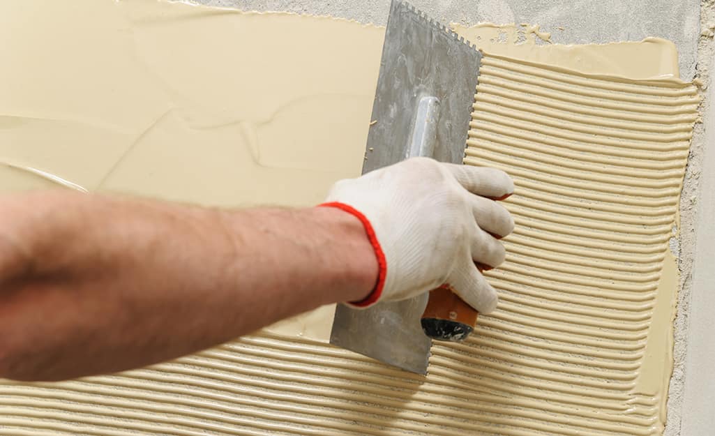 A person adds adhesive before installing flooring. A person adds adhesive before installing flooring.