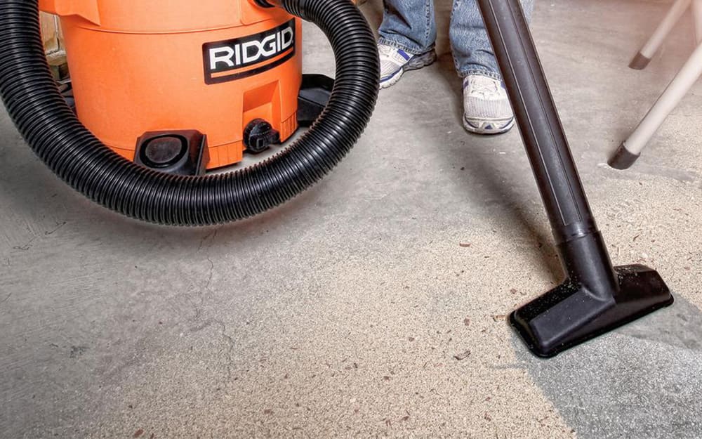 A person uses a vacuum to clean a concrete floor. A person uses a vacuum to clean a concrete floor.