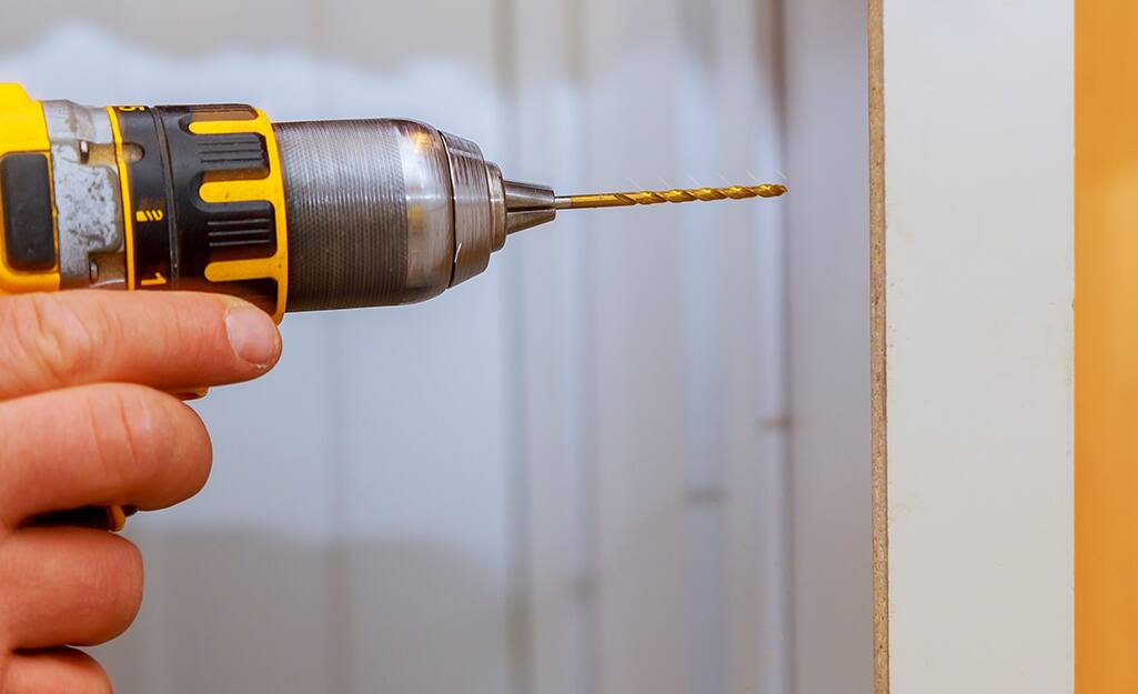 A person drills a cabinet screw. A person drills a cabinet screw.