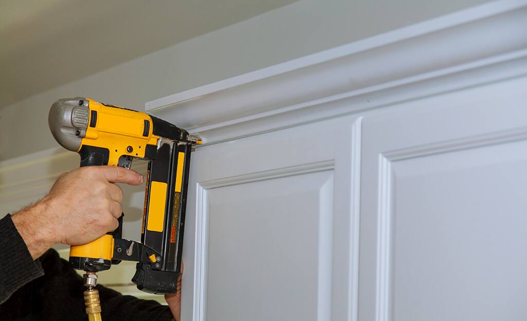 A person uses a nailer to hang a valance. A person uses a nailer to hang a valance.