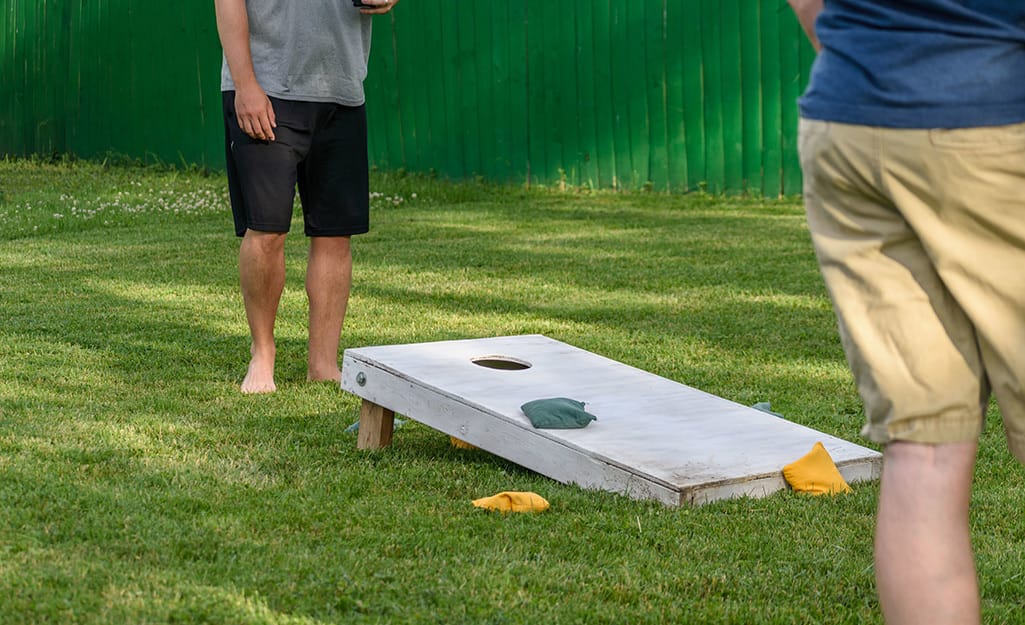 Two people playing cornhole on a lawn. Two people playing cornhole on a lawn.