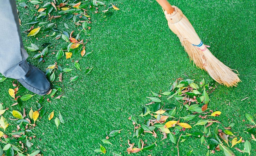 Someone sweeping leaves off a putting green made of synthetic turf. Someone sweeping leaves off a putting green made of synthetic turf.