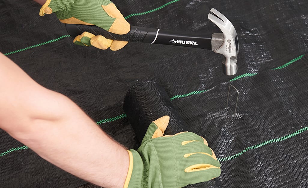 Someone using a hammer and garden staples to hold landscape fabric over the site for a Zen garden. Someone using a hammer and garden staples to hold landscape fabric over the site for a Zen garden.