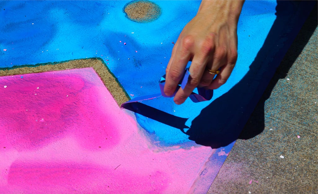 A woman removes painter's tape from her sidewalk chalk painting. A woman removes painter's tape from her sidewalk chalk painting.