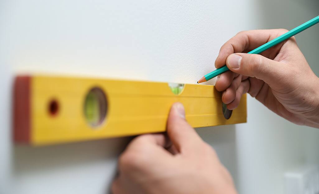 Someone using a level to mark pilot holes on a wall. Someone using a level to mark pilot holes on a wall.