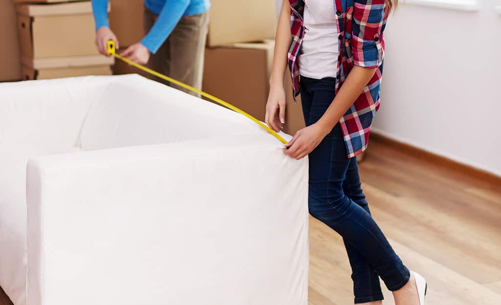 Two people measure the back of a couch. Two people measure the back of a couch.
