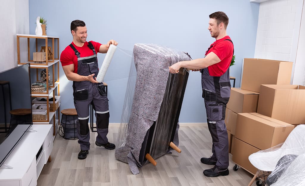 Two professional movers wrap a couch. Two professional movers wrap a couch.
