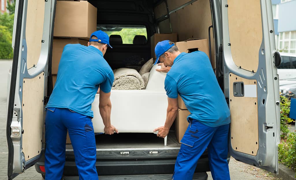 Two movers put a couch into the back of a moving van. Two movers put a couch into the back of a moving van.