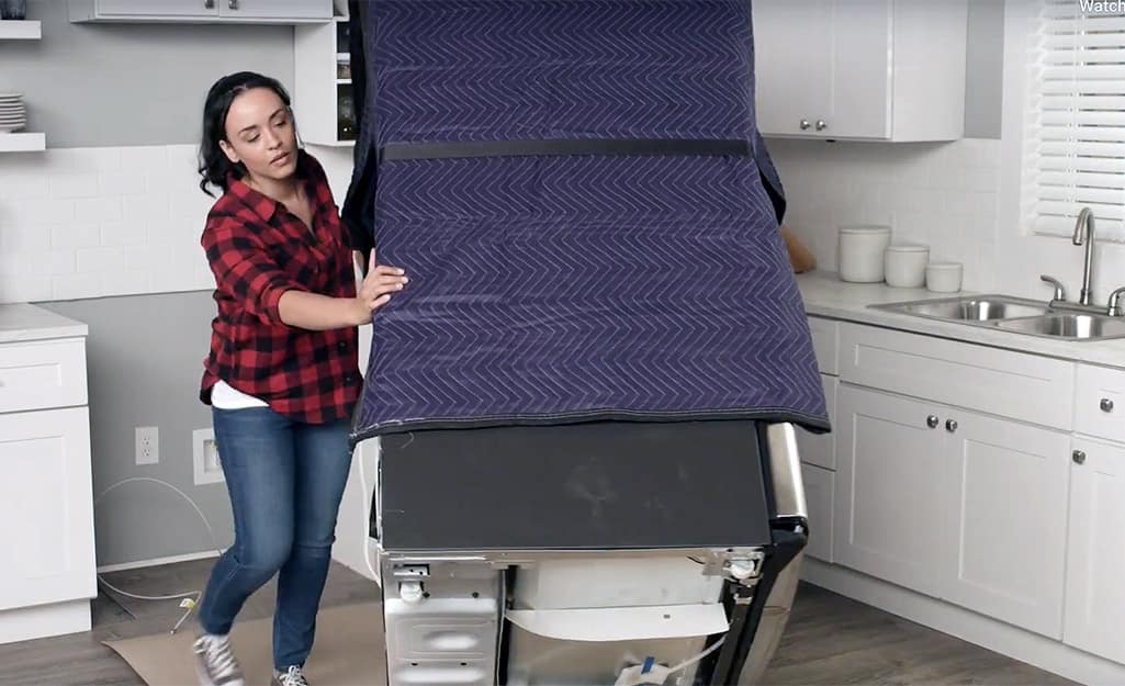 A person assisting with moving a refrigerator strapped to a dolly. A person assisting with moving a refrigerator strapped to a dolly.