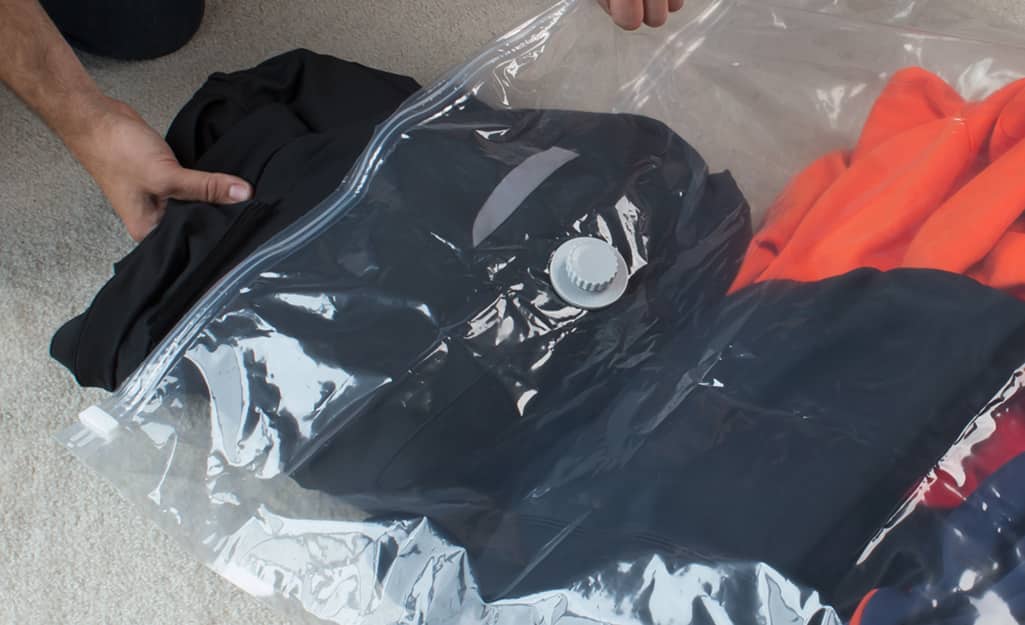 Someone placing bulky clothing into a vacuum bag. Someone placing bulky clothing into a vacuum bag.