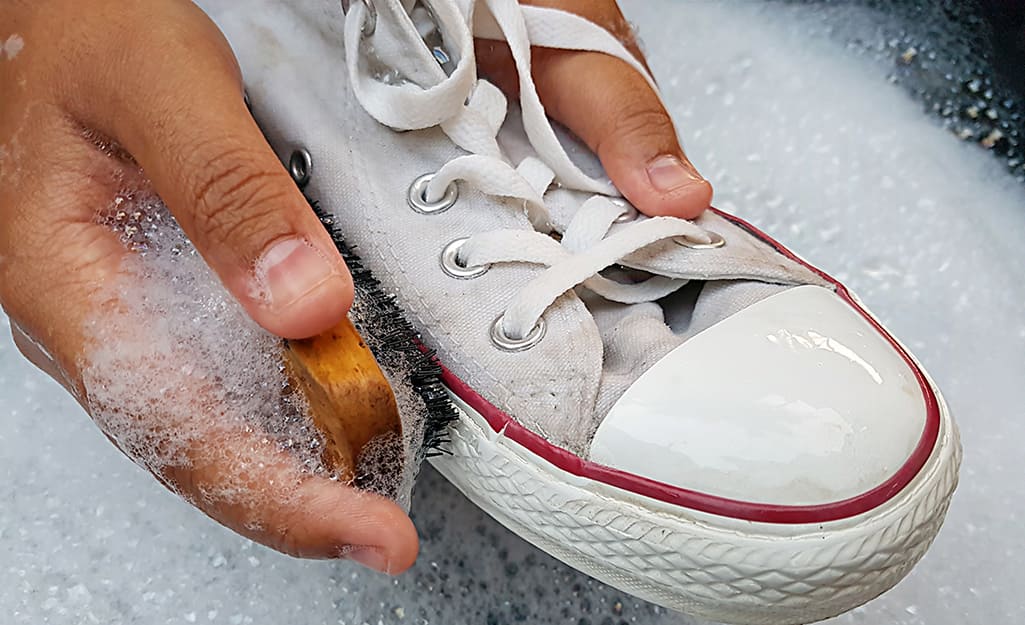 Person washing athletic shoes with brush and soapy water. Person washing athletic shoes with brush and soapy water.