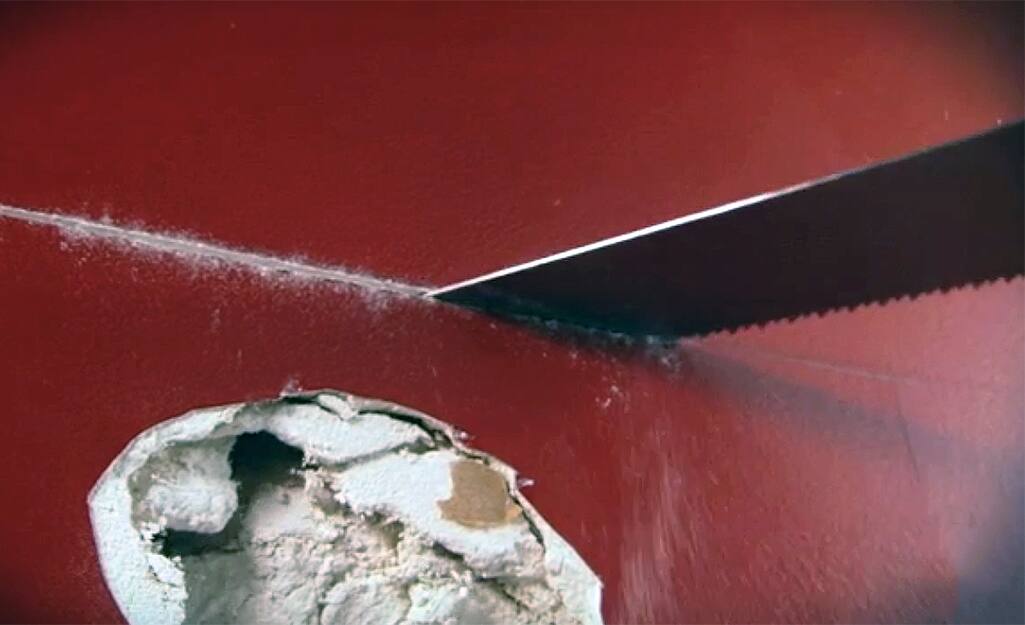 A person cutting around a hole in drywall with a drywall saw. A person cutting around a hole in drywall with a drywall saw.