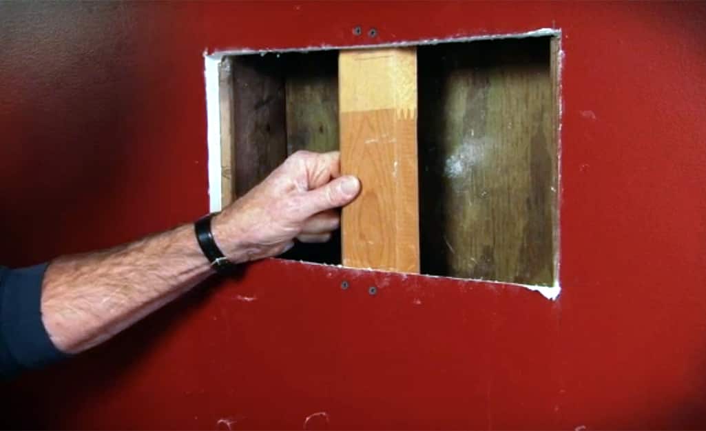 A person installing a wood support behind an opening in drywall. A person installing a wood support behind an opening in drywall.
