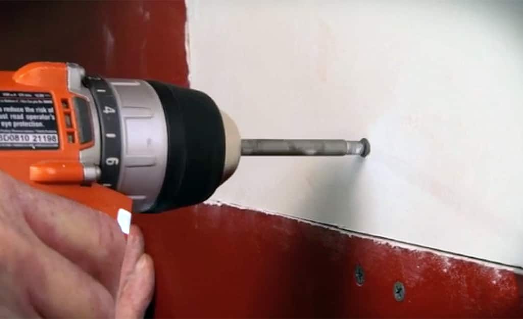 A person drilling a drywall screw into a drywall patch in the wall. A person drilling a drywall screw into a drywall patch in the wall.
