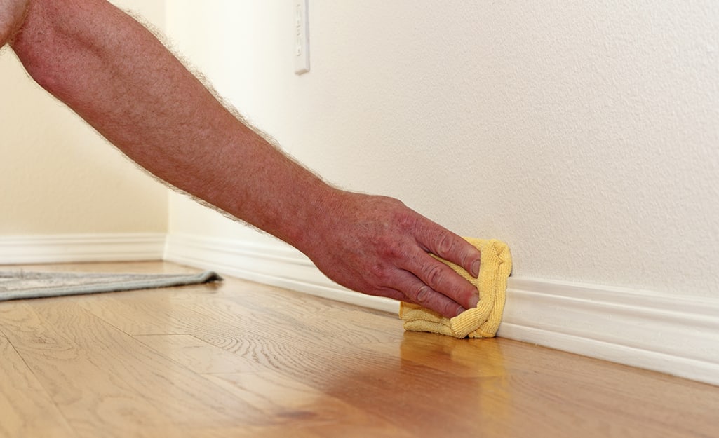 A person cleaning baseboards with a cloth. A person cleaning baseboards with a cloth.
