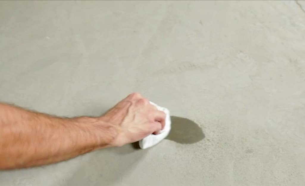A person wiping water from a concrete subfloor. A person wiping water from a concrete subfloor.