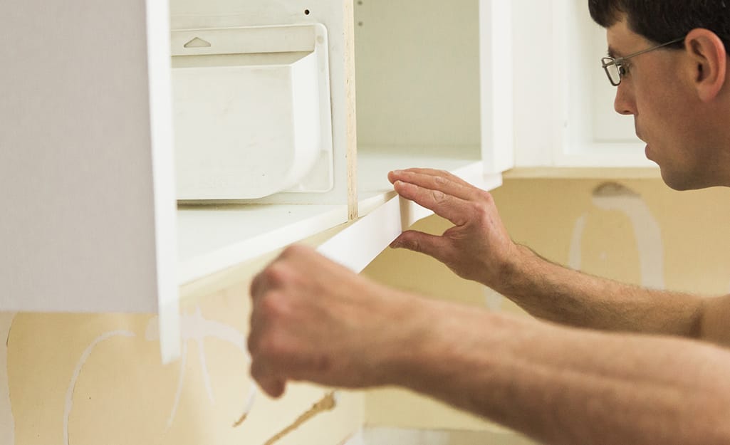 A person applies veneer to the horizontal edge of a kitchen cabinet. A person applies veneer to the horizontal edge of a kitchen cabinet.