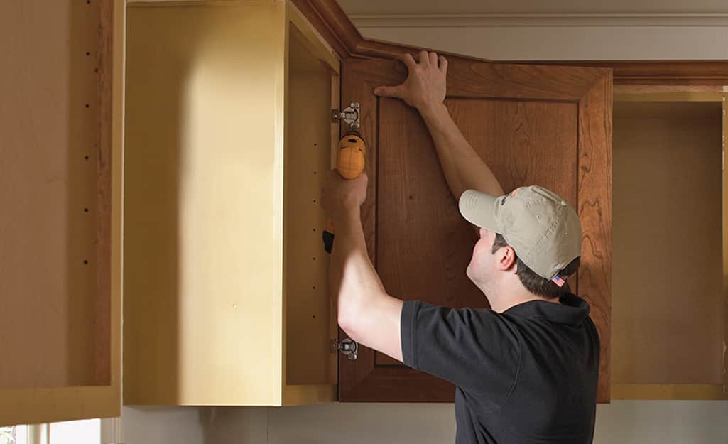 A person reattaches a door to a kitchen cabinet. A person reattaches a door to a kitchen cabinet.