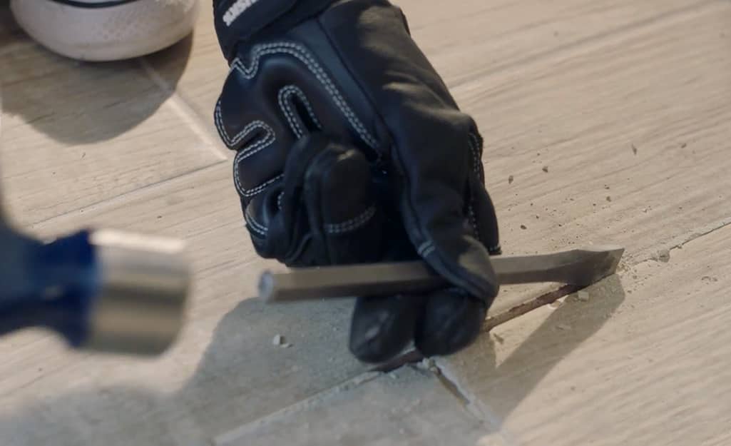 Someone removing tile grout with a chisel. Someone removing tile grout with a chisel.