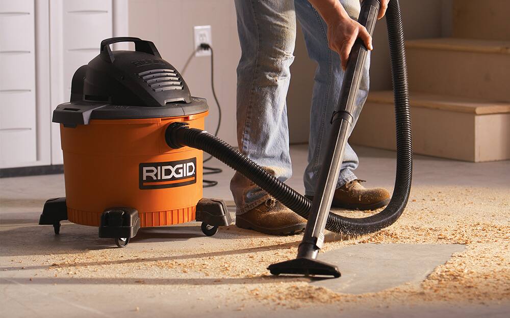 person vacuuming up wood shavings and dust