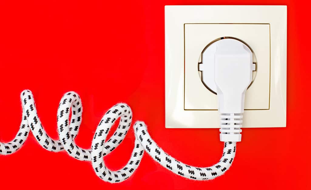 A fabric-covered power cord is plugged into an outlet. A fabric-covered power cord is plugged into an outlet.