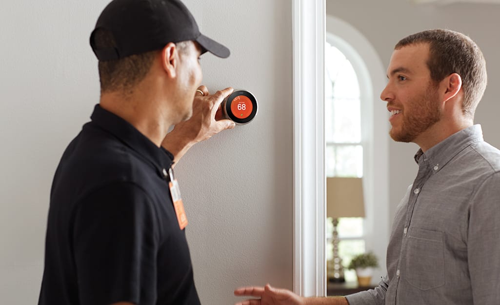 A Home Depot associate standing next to a homeowner and adjusting a smart thermostat on a wall. A Home Depot associate standing next to a homeowner and adjusting a smart thermostat on a wall.