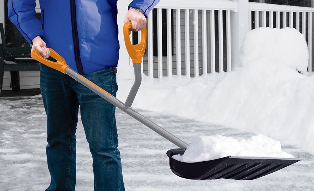 A person holding a snow shovel with an ergonomic handle. A person holding a snow shovel with an ergonomic handle.