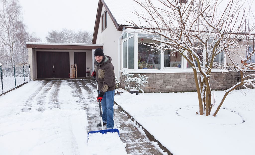 A person using a snow shovel to remove snow from a driveway. A person using a snow shovel to remove snow from a driveway.