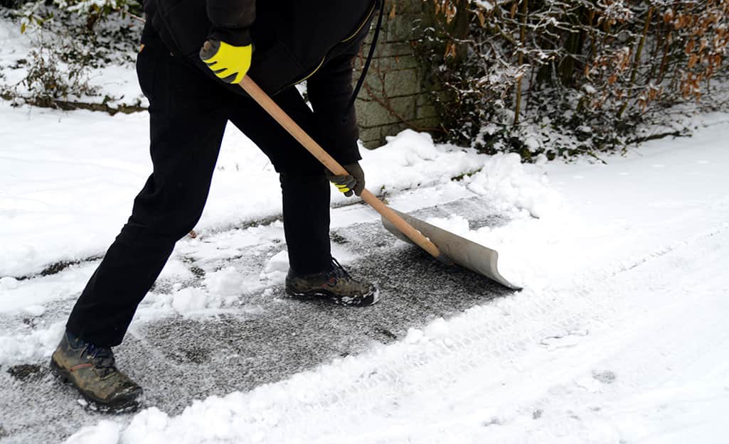 A person using a snow shovel to remove snow from a driveway. A person using a snow shovel to remove snow from a driveway.