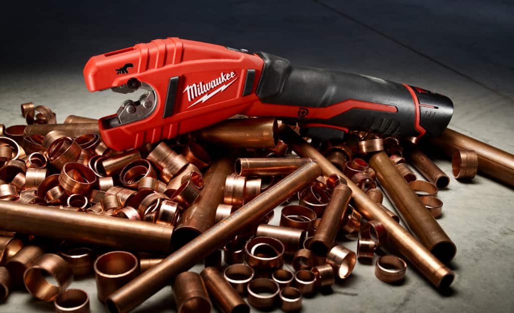 A pipe cutter sits atop a pile of copper pipe and copper pipe fittings. A pipe cutter sits atop a pile of copper pipe and copper pipe fittings.