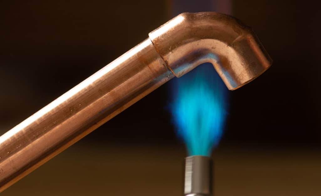 A soldering iron flame heats a copper fitting. A soldering iron flame heats a copper fitting.