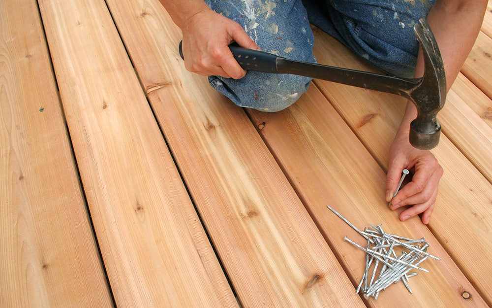 A person hammers a nail into a deck board. A person hammers a nail into a deck board.