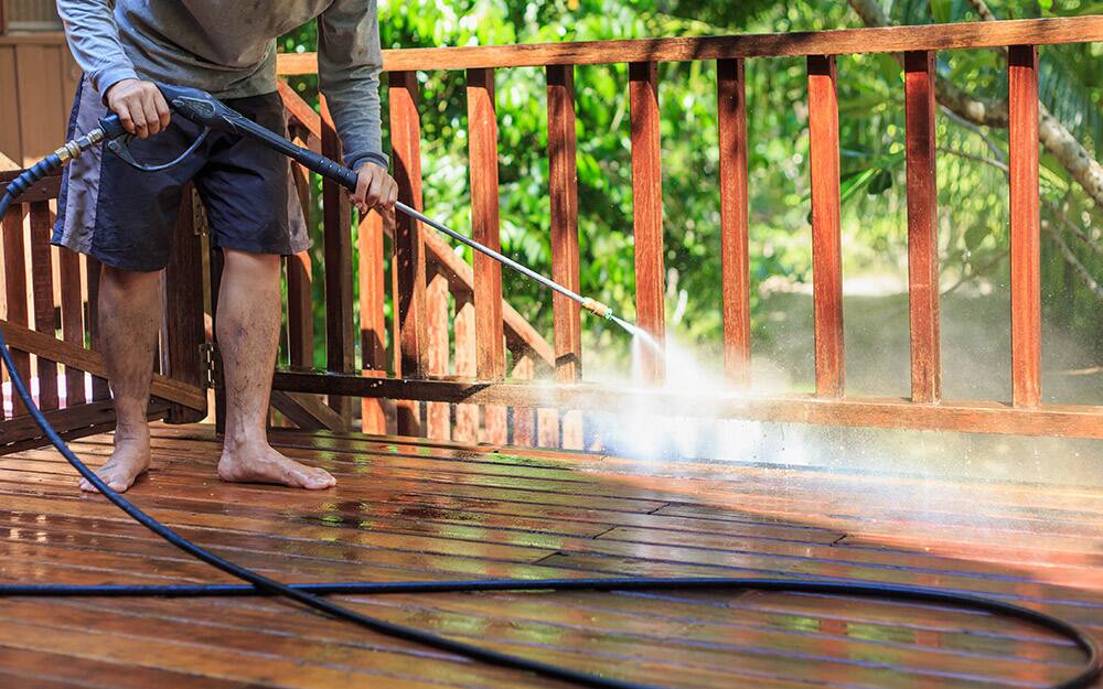 A person washes a deck with a sprayer. A person washes a deck with a sprayer.