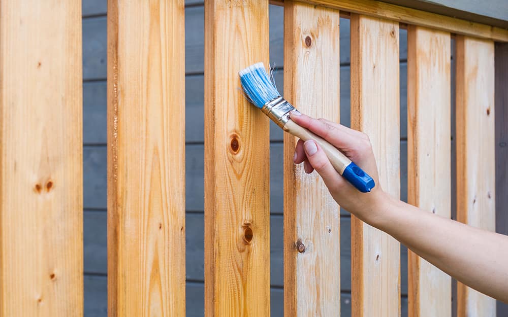 A person stains the balusters of a deck with a brush. A person stains the balusters of a deck with a brush.