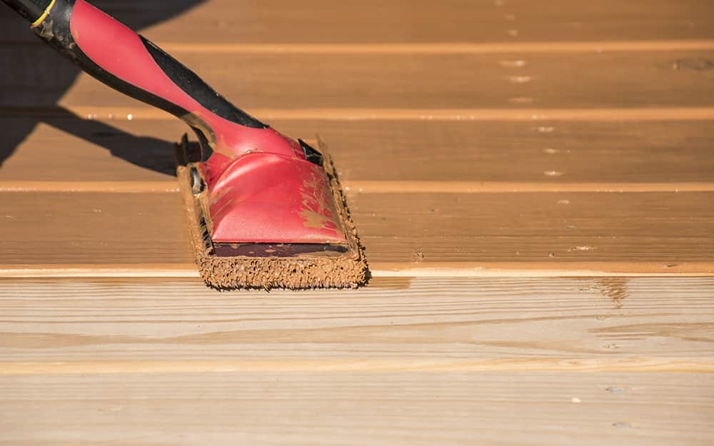 A person stains deck boards with a pad applicator. A person stains deck boards with a pad applicator.