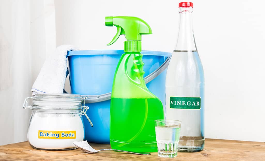 A container of baking soda sits next to a blue bucket, a green spray bottle and a bottle of vinegar A container of baking soda sits next to a blue bucket, a green spray bottle and a bottle of vinegar