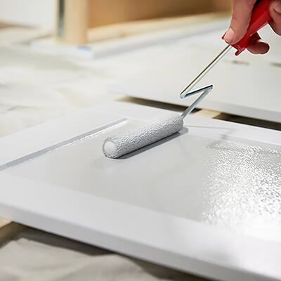A person painting a cabinet white with a paint roller.