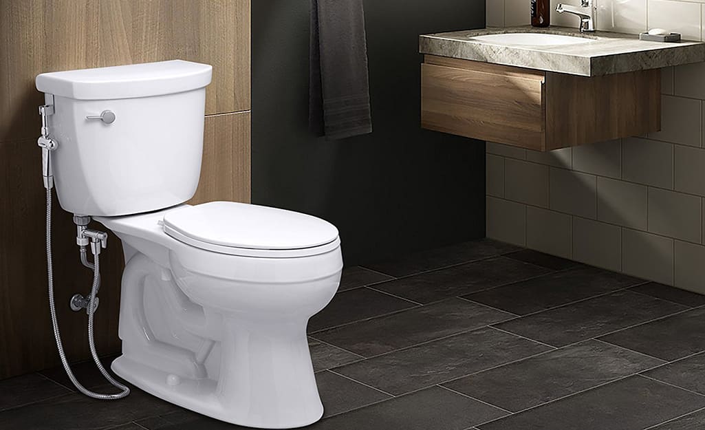 A hand-held bidet sprayer is installed on the side of a toilet in a bathroom. A hand-held bidet sprayer is installed on the side of a toilet in a bathroom.