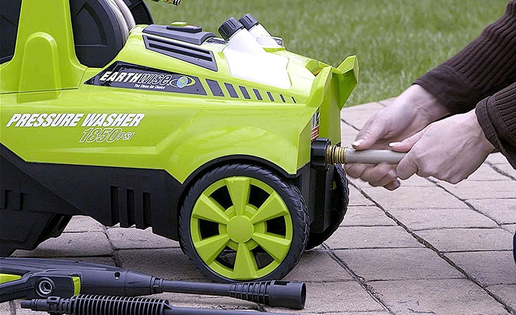 A person removes a garden hose from the pressure washer's water inlet. A person removes a garden hose from the pressure washer's water inlet.