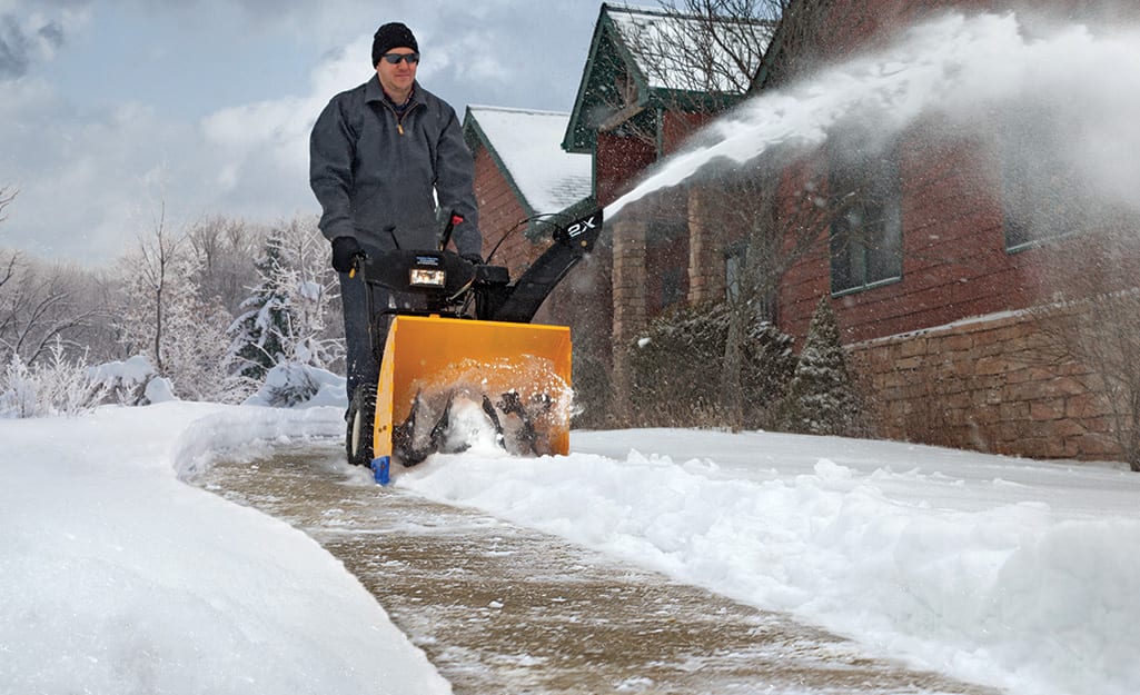 A person using a snow blower to clear snow from a sidewalk. A person using a snow blower to clear snow from a sidewalk.