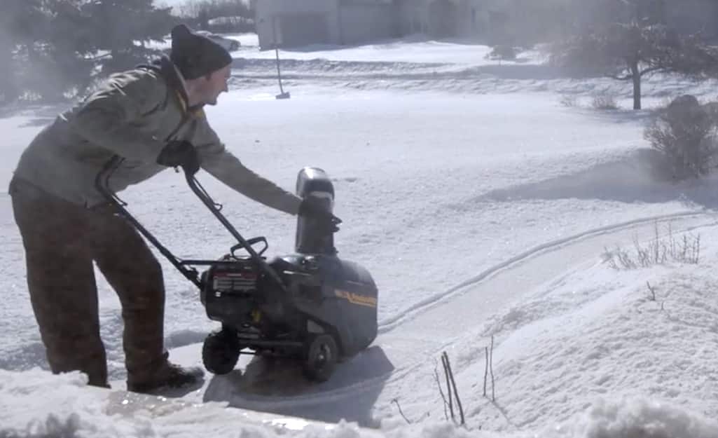 A person making adjustments to a snow blower. A person making adjustments to a snow blower.