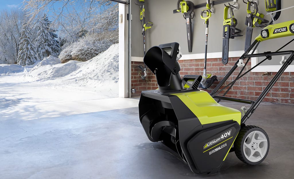 A battery powered snow blower stored in a garage. A battery powered snow blower stored in a garage.