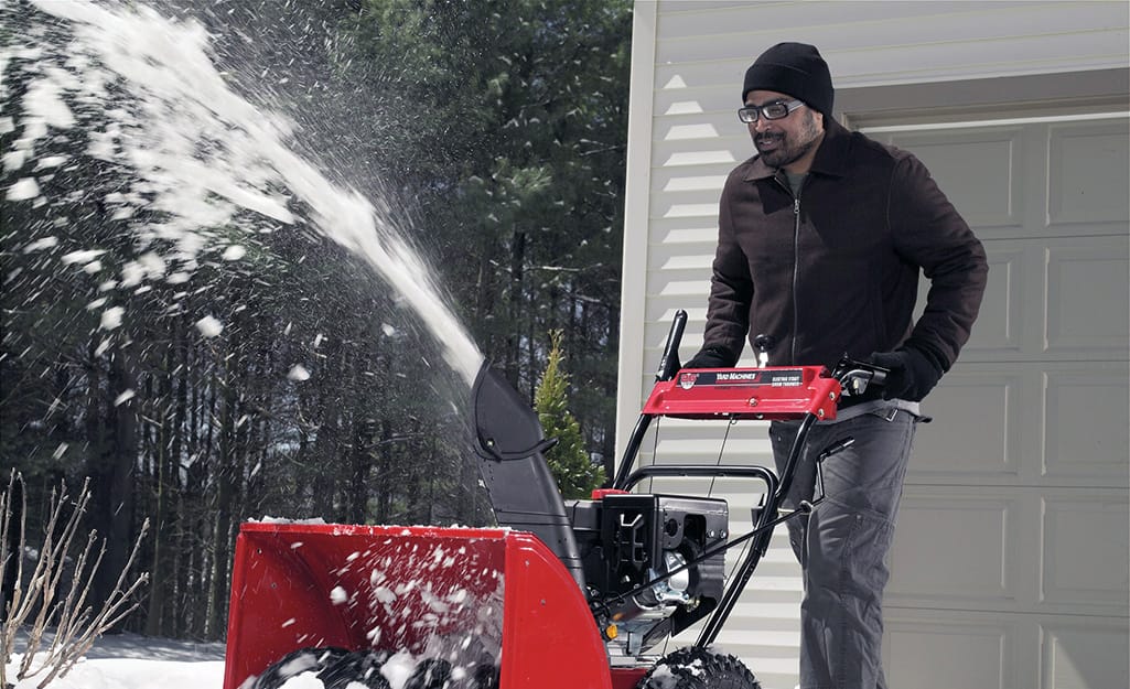 A person wearing safety goggles using a snow blower. A person wearing safety goggles using a snow blower.