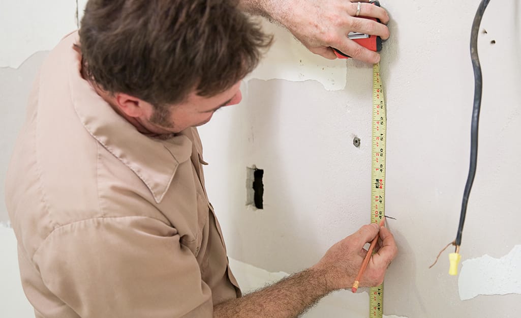 A person using a tape measure to mark for the outlet. A person using a tape measure to mark for the outlet.