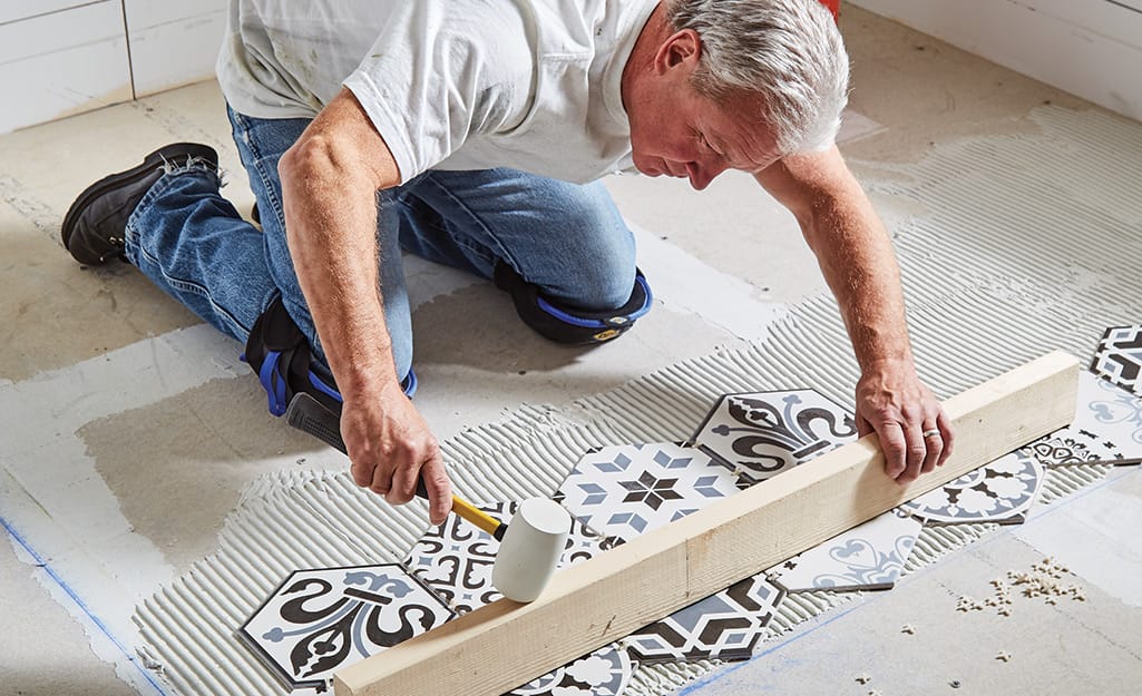Man leveling rows of tile using a mallet and wood board. Man leveling rows of tile using a mallet and wood board.