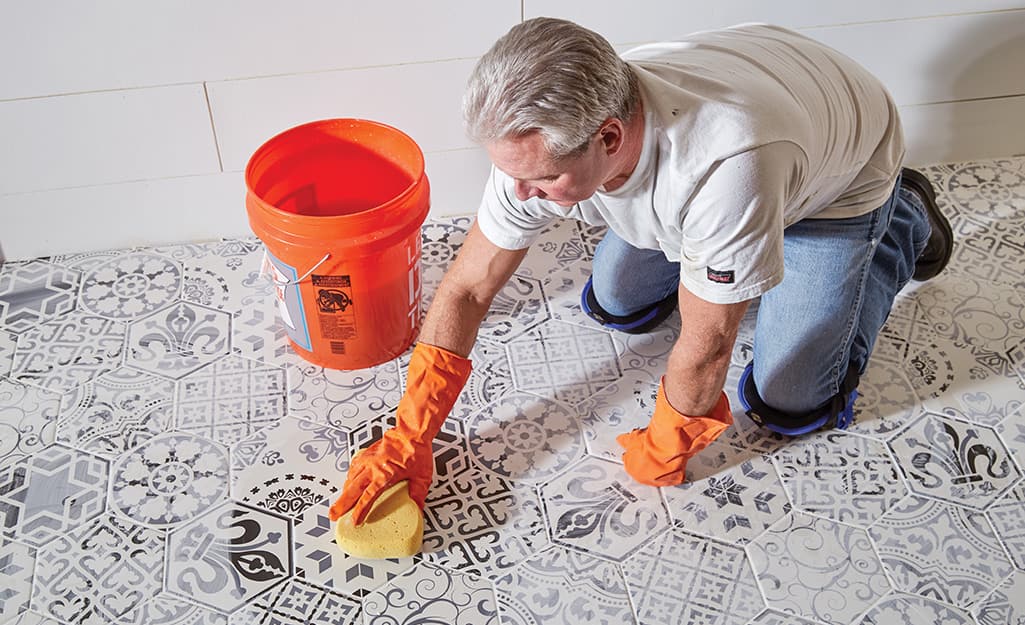 Person cleaning excess grout from tiles with sponge. Person cleaning excess grout from tiles with sponge.